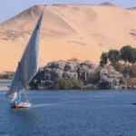 Felucca navegando por el Nilo junto a dunas de arena en Asuán