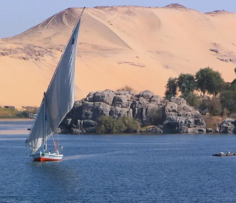Felucca navegando por el Nilo junto a dunas de arena en Asuán