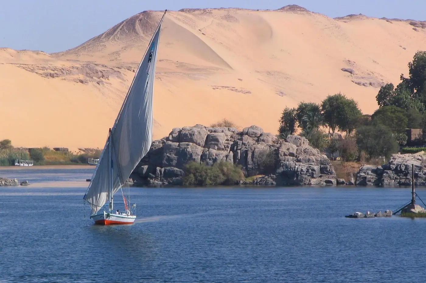 Felucca navegando por el Nilo junto a dunas de arena en Asuán